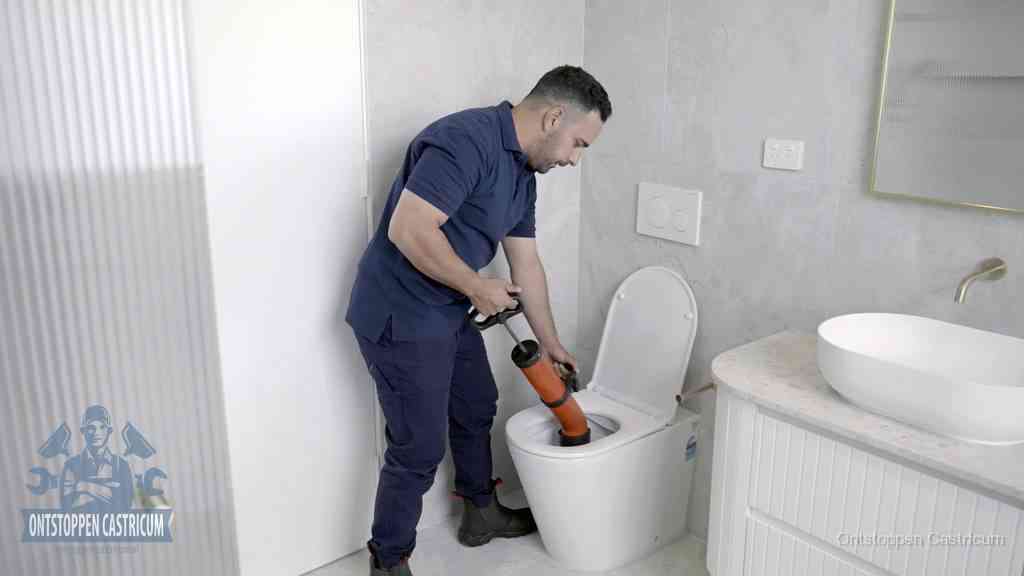 Een monteur buigt over een wandcloset en duwt met de hand een persluchtontstopper in de toiletpot om de verstopping handmatig los te maken in Castricum