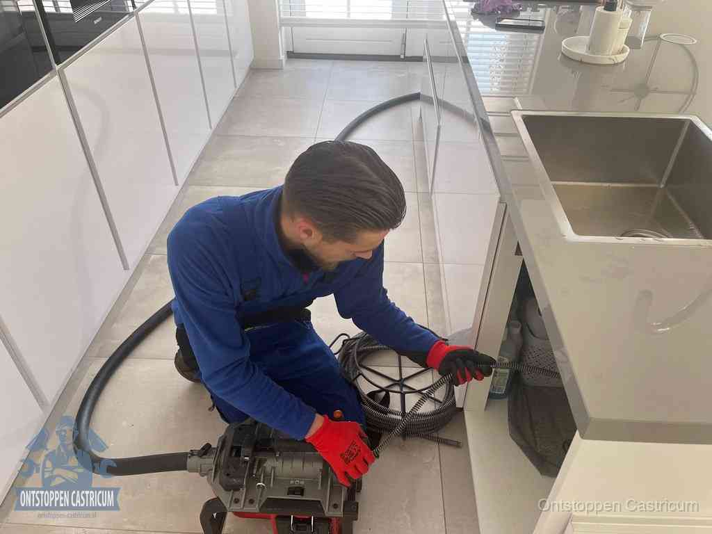 Een monteur ontstopt de keukenafvoer onder de spoelbak met een elektrische veermachine in Castricum
