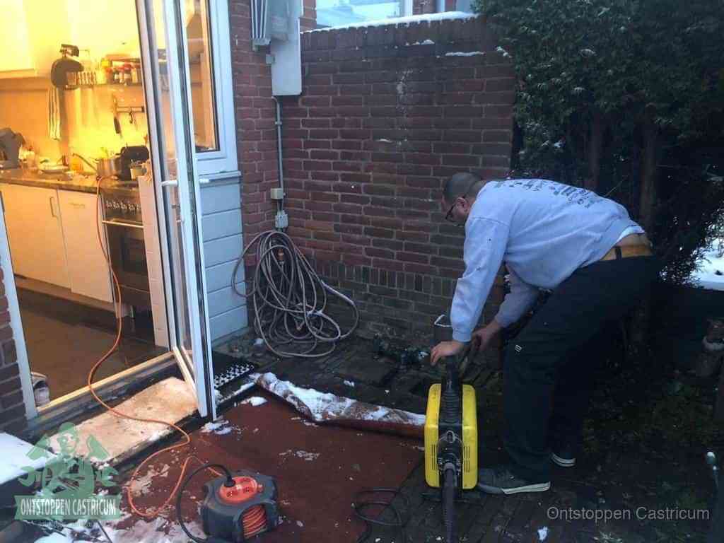 Een monteur werkt buiten bij een open riool-/grondput met een elektrische ontstoppingsmachine om een verborgen afvoerprobleem op te sporen in Castricum