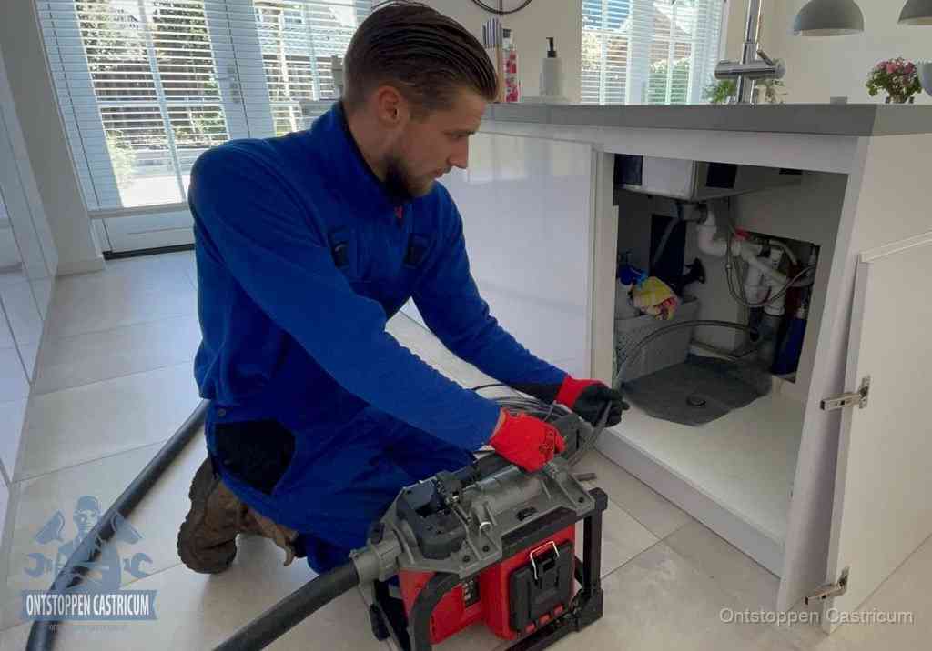 Een monteur voert een professionele elektrische ontstoppingsmachine in de afvoer onder de spoelbak tijdens het gootsteen ontstoppen in Castricum